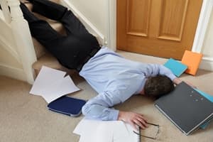 A man in business attire lies face down at the bottom of a staircase, surrounded by scattered papers, folders, and a pair of glasses, indicating a slip and fall accident while carrying work materials.