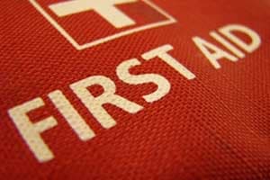 Close-up of a red first aid kit with a white cross and "FIRST AID" printed in bold white letters on the textured fabric, essential for workplaces handling work-related injuries claims.